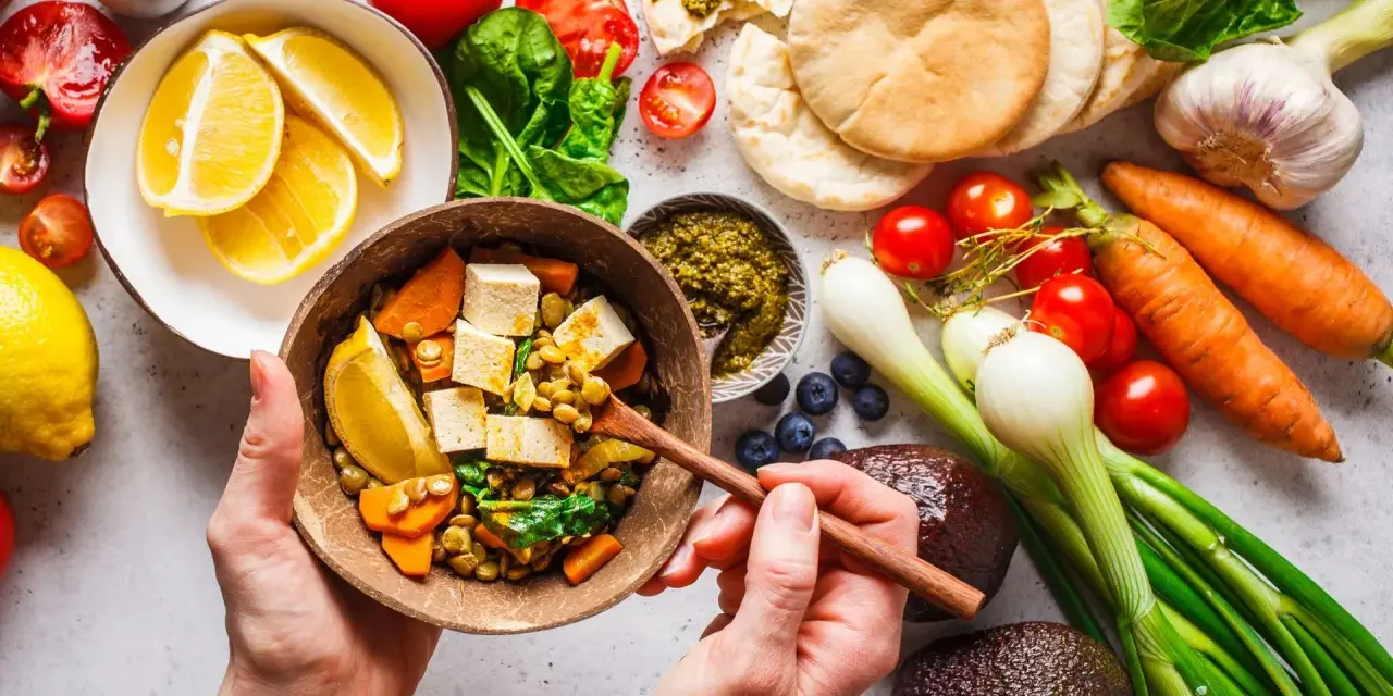 Zdrowa dieta na stawy: miska pełna soczewicy, tofu, warzyw i cytryny. Obok składniki na pyszne danie: pomidory, marchew, awokado, czosnek, cebula, jagody, pesto i chlebki pita.