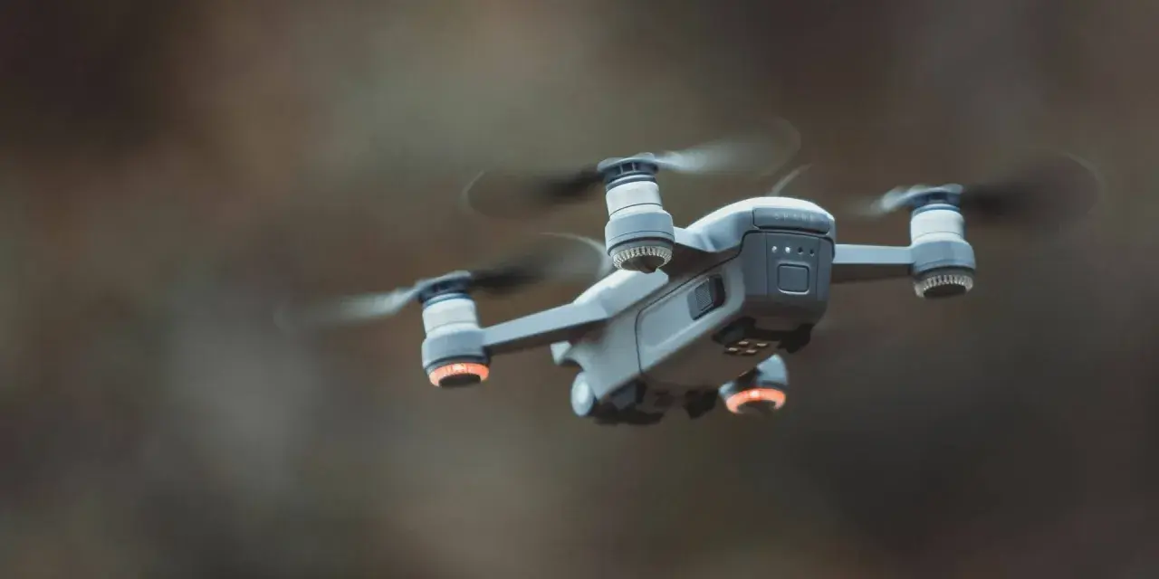 A drone hovers mid-air, its propellers a blur. Red anti-collision lights glow on its arms, ensuring safe flight.