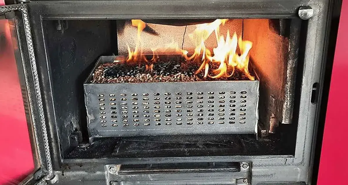 Estufa de pellets ardiendo dentro de un hueco de chimenea. El combustible se quema en una bandeja metálica perforada.