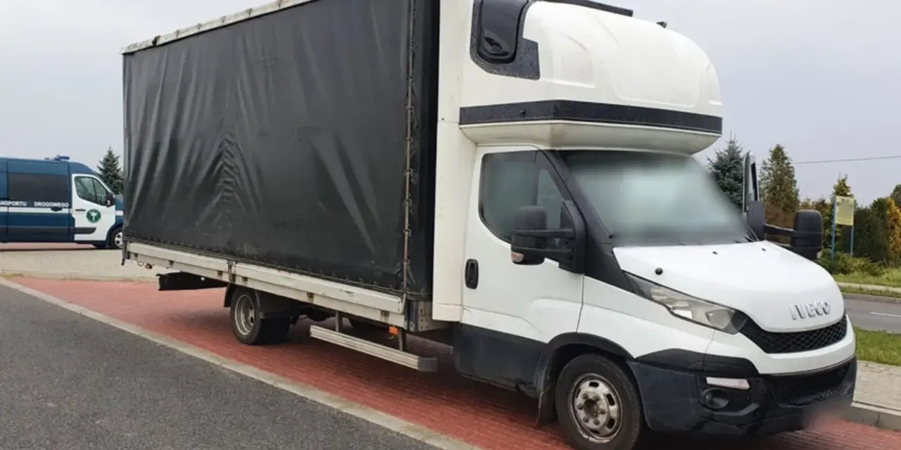 Biały bus Iveco z czarnym plandeką, ładowność 1,5 tony, stoi na czerwonej kostce brukowej.