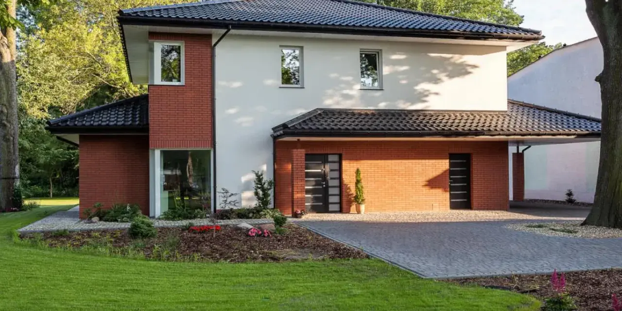 Nowoczesny dom z ceglanymi akcentami i eleganckim, czarnym dachem czterospadowym, otoczony zielenią.