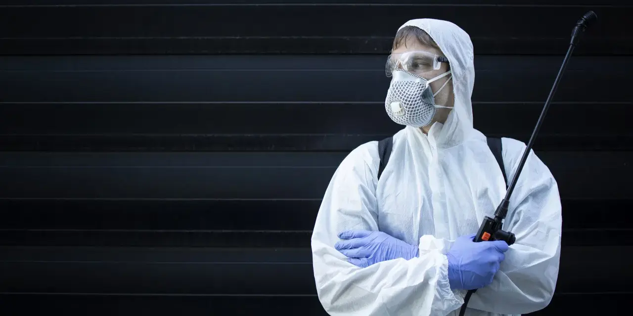 Persona con traje protector, mascarilla y gafas, sosteniendo un pulverizador. ¿Cuánto tiempo esperar después de fumigar?