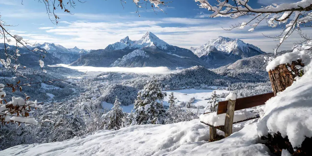 Ein verschneites Tal mit einem majestätischen Berg im Hintergrund. Eine Bank lädt zum Verweilen ein, perfekt für einen **ausflug im winter**.