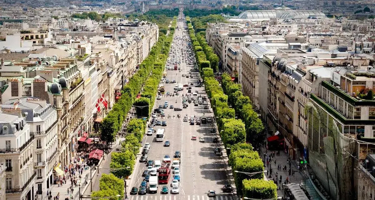 Vista aérea de la **Champs-Élysées** en París, con tráfico y peatones paseando entre los árboles y edificios.