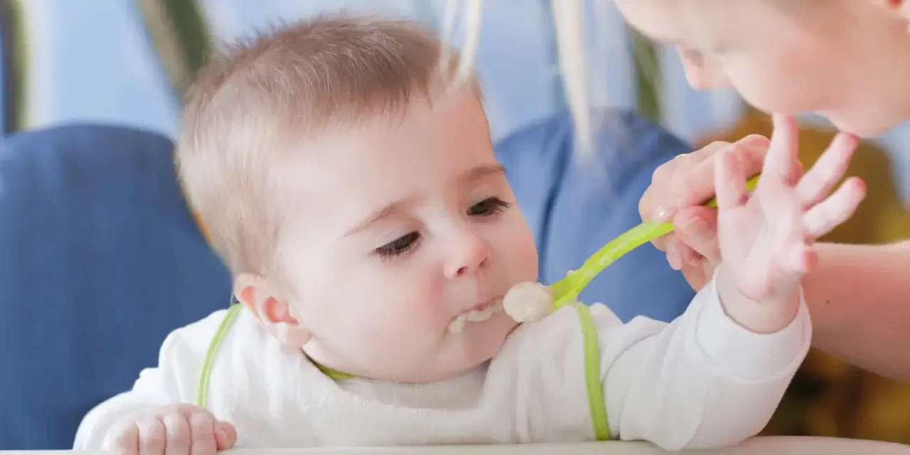 Mama karmi dziecko łyżeczką do karmienia niemowląt. Maluch z zaciekawieniem patrzy na jedzenie.
