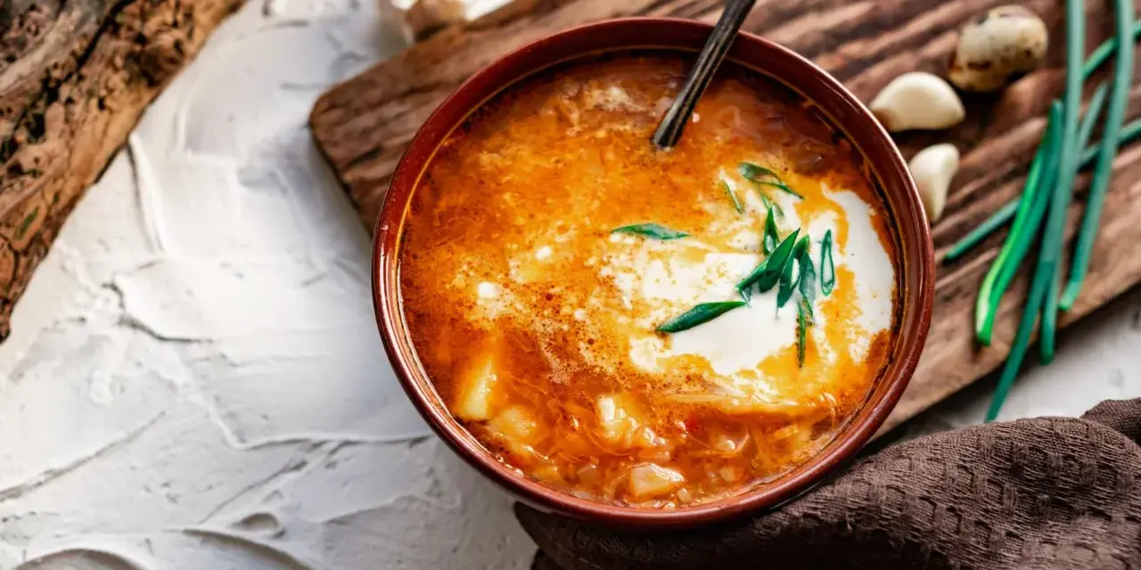 Un tazón de sopa de ajo con crema y cebolleta, acompañado de ajos y cebolletas.