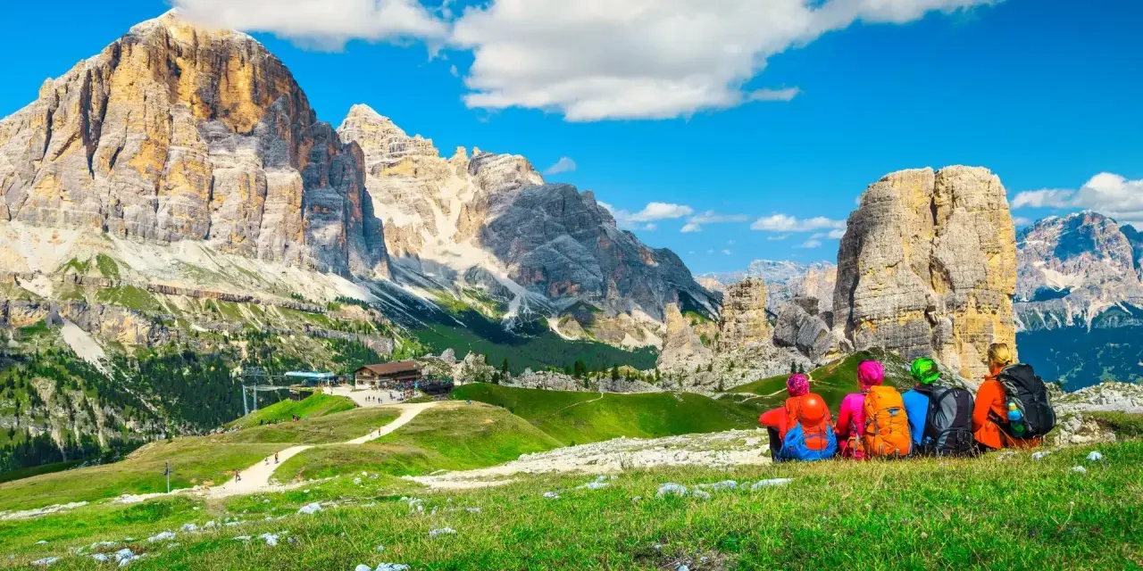 Quattro escursionisti ammirano un maestoso itinerario dolomiti, con cime imponenti e un rifugio alpino.