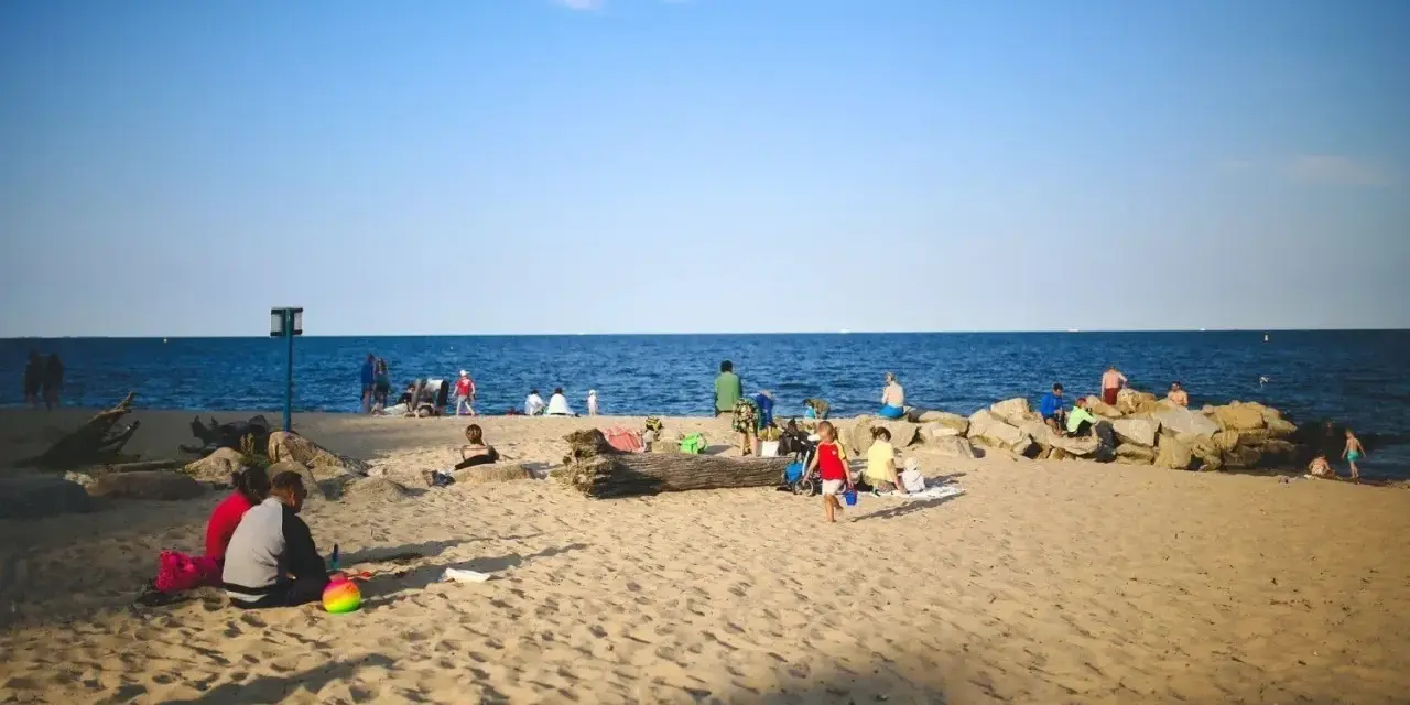 Ludzie odpoczywają na plaży, ciesząc się słońcem i morzem. Widać, ile Szczecin ma do morza – bliskość natury i relaks.