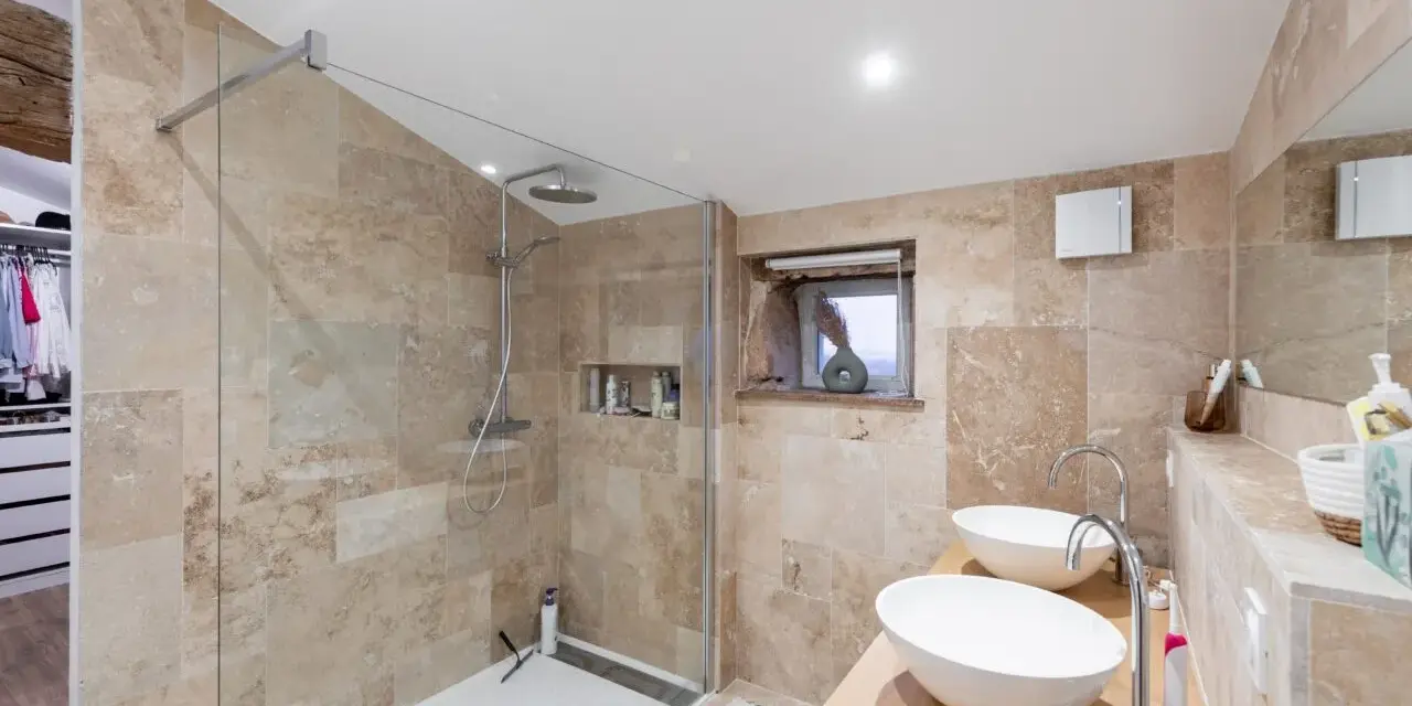 Salle de bain moderne avec douche à l'italienne, double vasque et carrelage en pierre naturelle. Un projet réussi pour refaire la salle de bain.