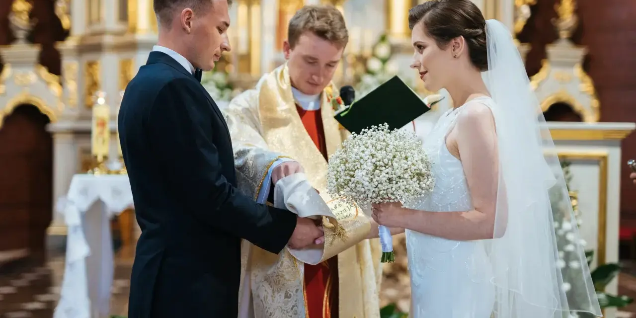 Panna młoda w welonie i z bukietem, pan młody w garniturze, podczas ceremonii ślubnej w kościele.