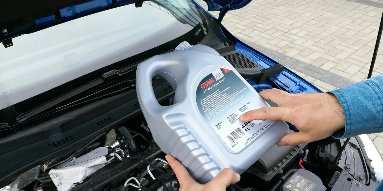 Osoba trzymająca kanister oleju silnikowego TITAN GT1 PRO C-3 SAE 5W-30 nad silnikiem. Czy można mieszać oleje silnikowe? Sprawdź specyfikacje!