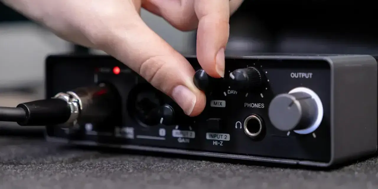 Dłoń reguluje pokrętło miksu na interfejsie audio, przygotowując wyjście liniowe do pracy.
