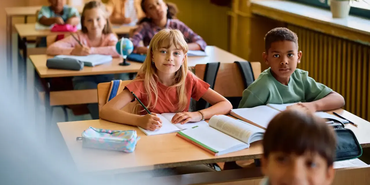 Dzieci w klasie skupione na lekcji. Uczennica pisze w zeszycie, obok niej leży piórnik. To pokazuje, co na koncentrację u dzieci: nauka i zaangażowanie.