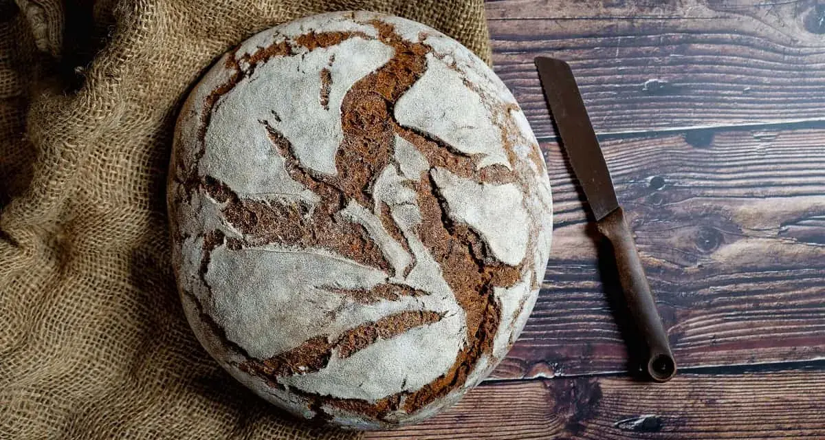 Pan casero rústico sobre arpillera, listo para cortar con un cuchillo. Una delicia para tu receta de pan casero.