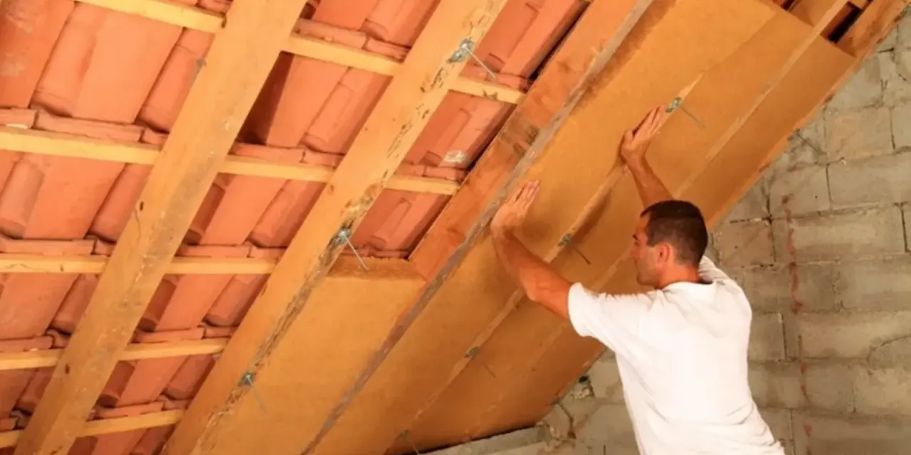 Operaio installa pannelli per la coibentazione del tetto in legno, migliorando l'isolamento termico.