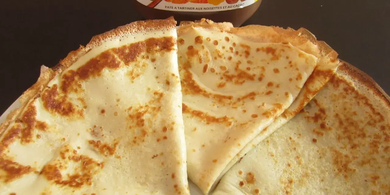 Crêpes dorées prêtes à être garnies, avec un pot de Nutella en arrière-plan. Une recette facile pour des crêpes maison !