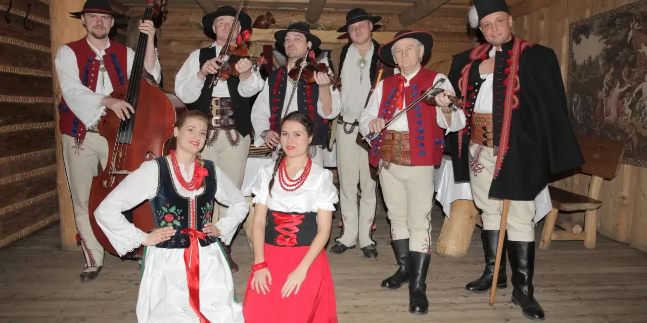 Zespół góralski w strojach ludowych, z instrumentami. Wśród nich skrzypkowie, basista i panie w tradycyjnych sukniach.