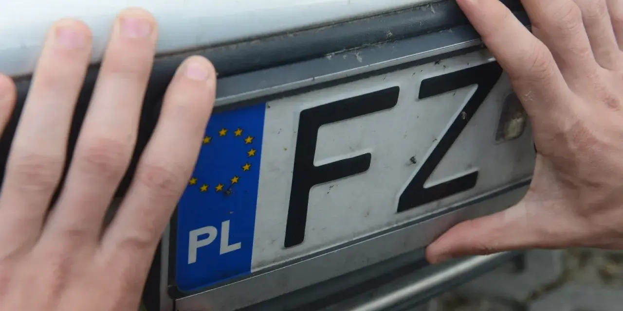 Dwie dłonie trzymają polską tablicę rejestracyjną z literami FZ.
