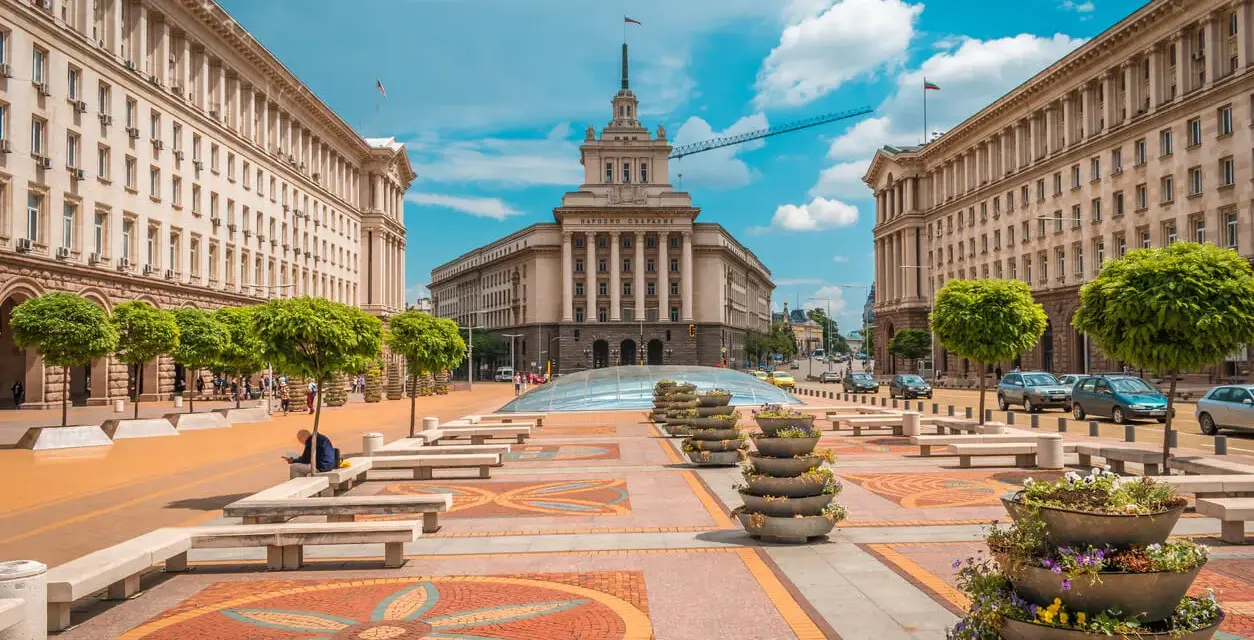 Słoneczna pogoda w Bułgarii w lipcu. Sofia, plac przed budynkiem Narodowego Zgromadzenia, z drzewami i kwiatami.