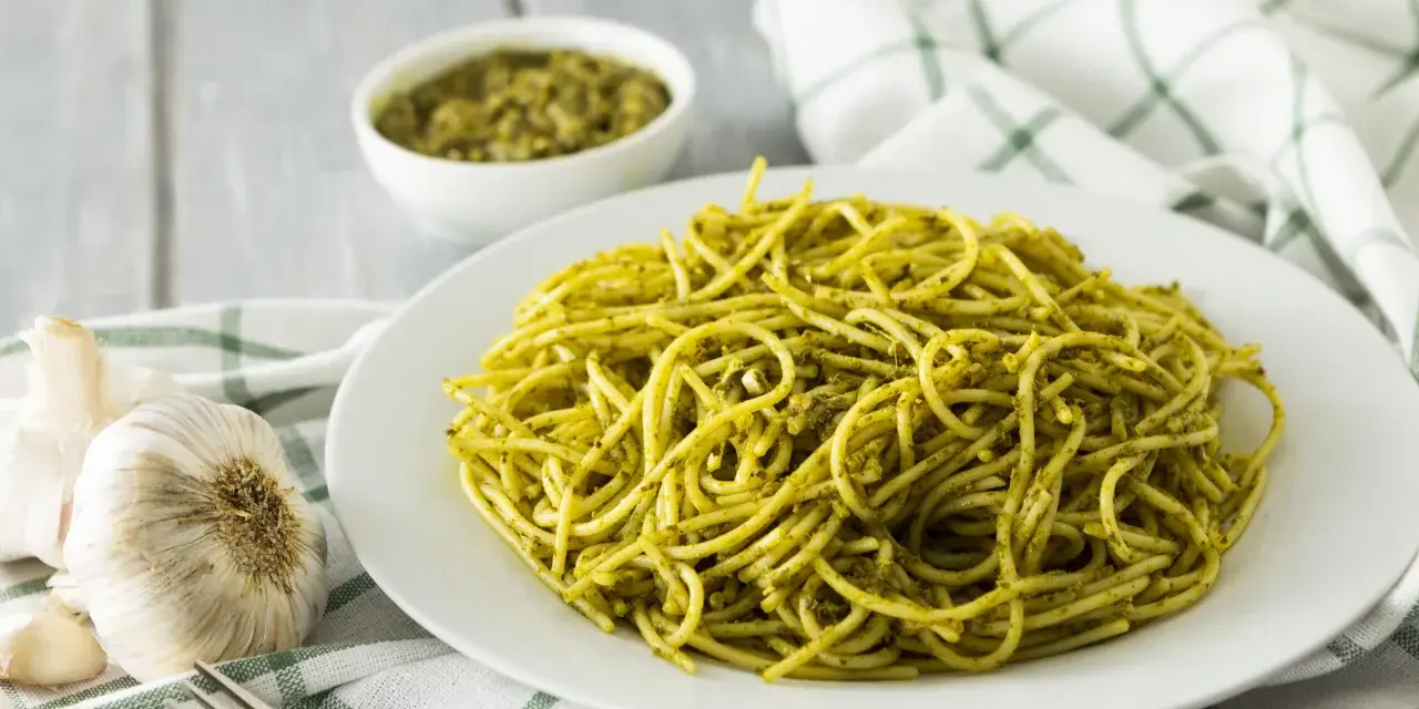 Pyszny makaron z pesto, podany na białym talerzu, obok czosnku i miseczki z sosem.