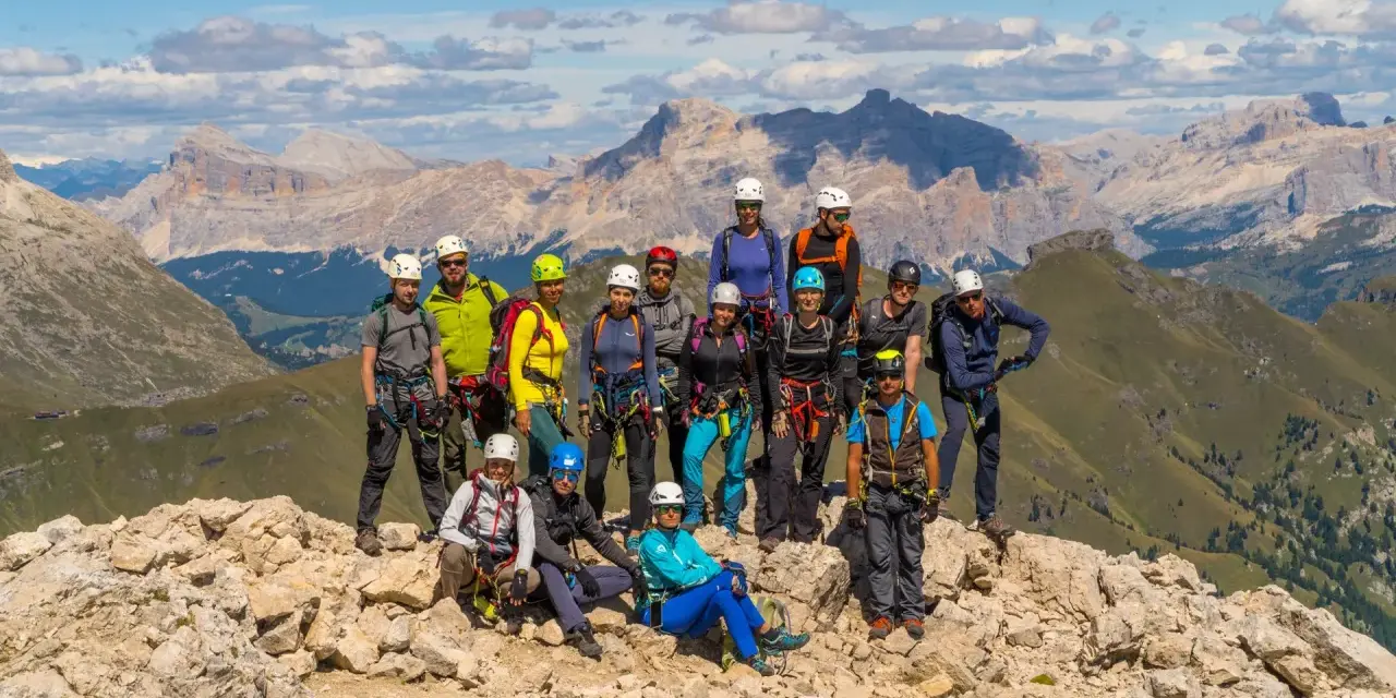 Grupa turystów w sprzęcie wspinaczkowym pozuje na tle górskich krajobrazów Dolomitów. To wspaniała przygoda na via ferrata Dolomity!