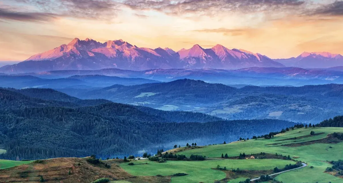 Tatry o zachodzie słońca, jedno z **10 najpiękniejszych miejsc w Polsce**. Góry w odcieniach różu i fioletu, zielone wzgórza i lasy.