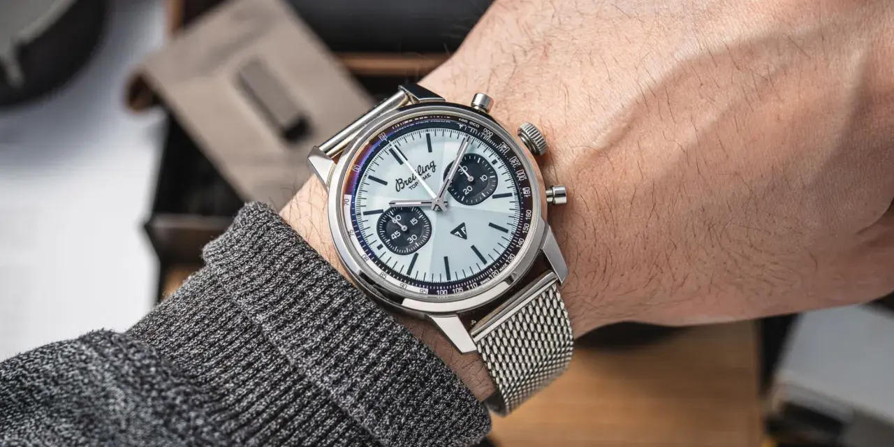 Mężczyzna prezentuje swój lśniący zegarek Breitling, gotowy do czyszczenia. Metalowa bransoleta i tarcza z chronografem błyszczą.