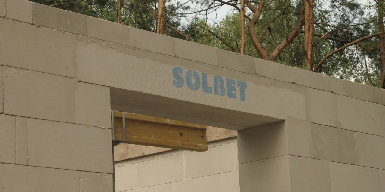 Ściana z bloczków betonowych z widocznym nadprożem marki SOLBET. Widać, jak nadproże ile powinno zachodzić, by zapewnić stabilność konstrukcji.