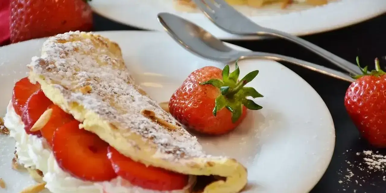 Pyszny omlet z białek z bitą śmietaną i truskawkami, posypany cukrem pudrem i płatkami migdałów.