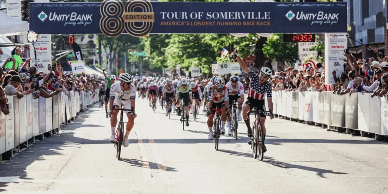 Cyclists race towards the finish line at the Tour of Somerville, America's longest-running bike race, with cheering crowds lining the street.