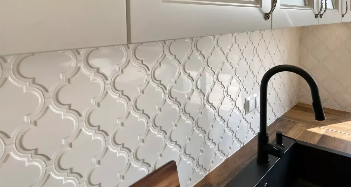 Białe, wypukłe płytki w kształcie arabeski tworzą elegancką mozaikę nad blatem kuchennym.