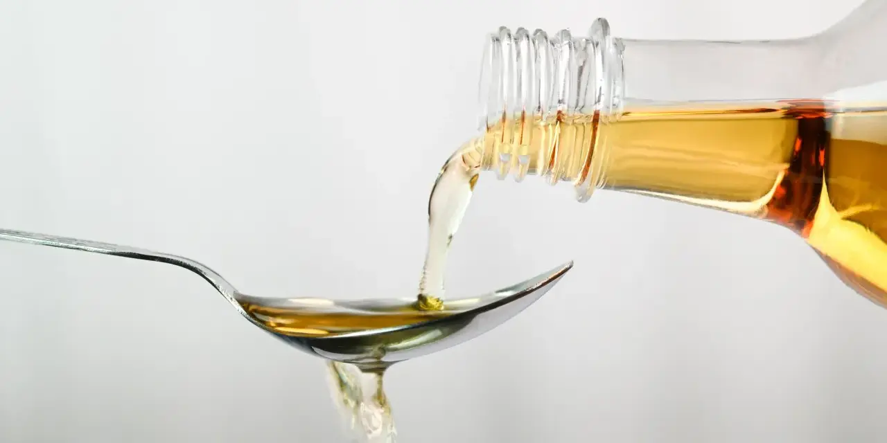 Apfelessig wird aus einer Flasche auf einen Löffel gegossen. Ein Tropfen für das Abnehmen.