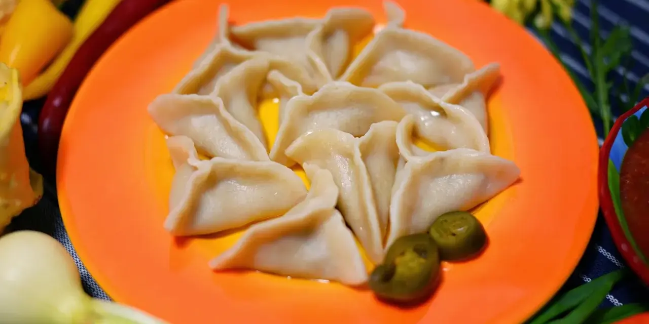 Pyszne pierogi meksykańskie, ułożone na pomarańczowym talerzu, z dodatkiem jalapeño i sosu.