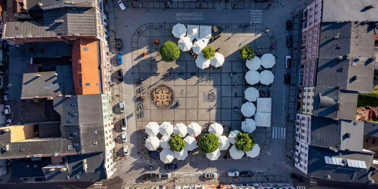 Widok z lotu ptaka na rynek w Kościerzynie, z białymi parasolami i zielenią.