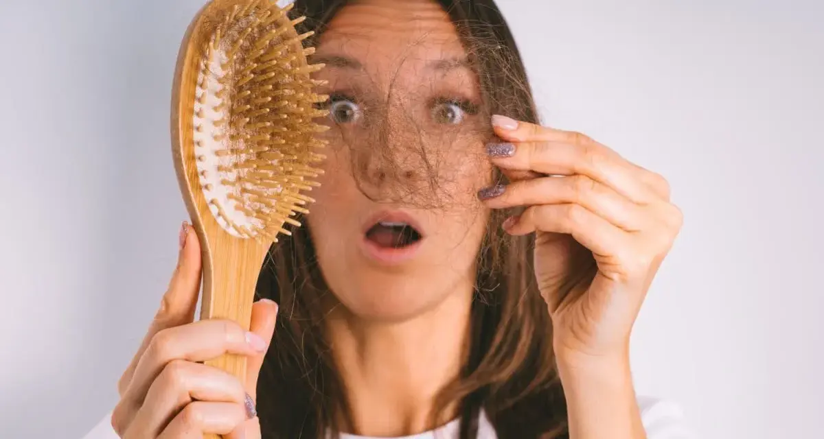 Frau mit erschrockenem Gesicht hält Haarbürste mit Haaren. Hoffnung auf progesteron haare wachsen wieder.