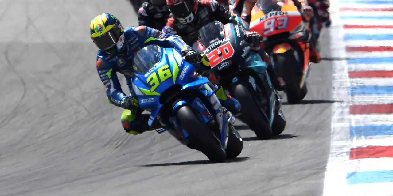 Pilotos de **MotoGP hoy** compiten en una carrera emocionante. El piloto con el número 36 en su Suzuki lidera, inclinado en una curva cerrada.