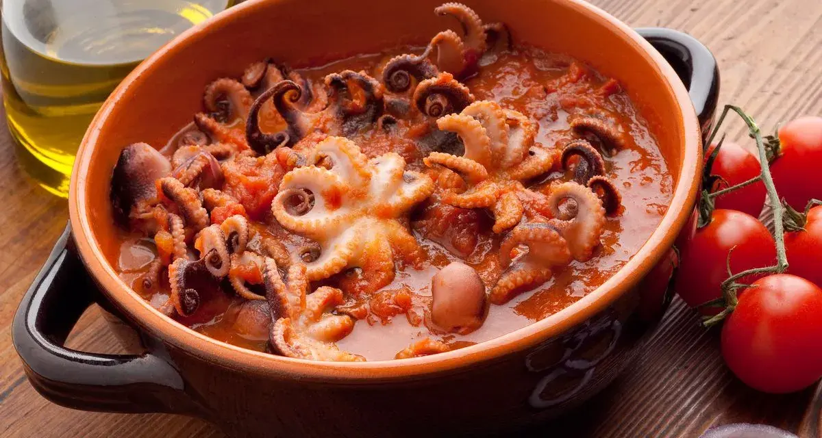 Polipetti in purgatorio, un piatto succulento con tentacoli che danzano in un sugo rosso, accompagnati da pomodorini freschi e cipolla.