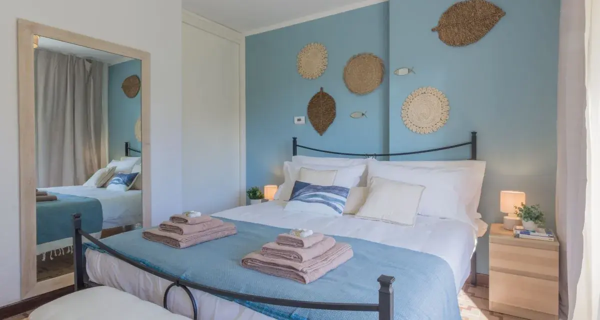 Idee camera da letto: letto matrimoniale con biancheria azzurra e cuscini bianchi, decorazioni a forma di foglia e pesci sulla parete blu.