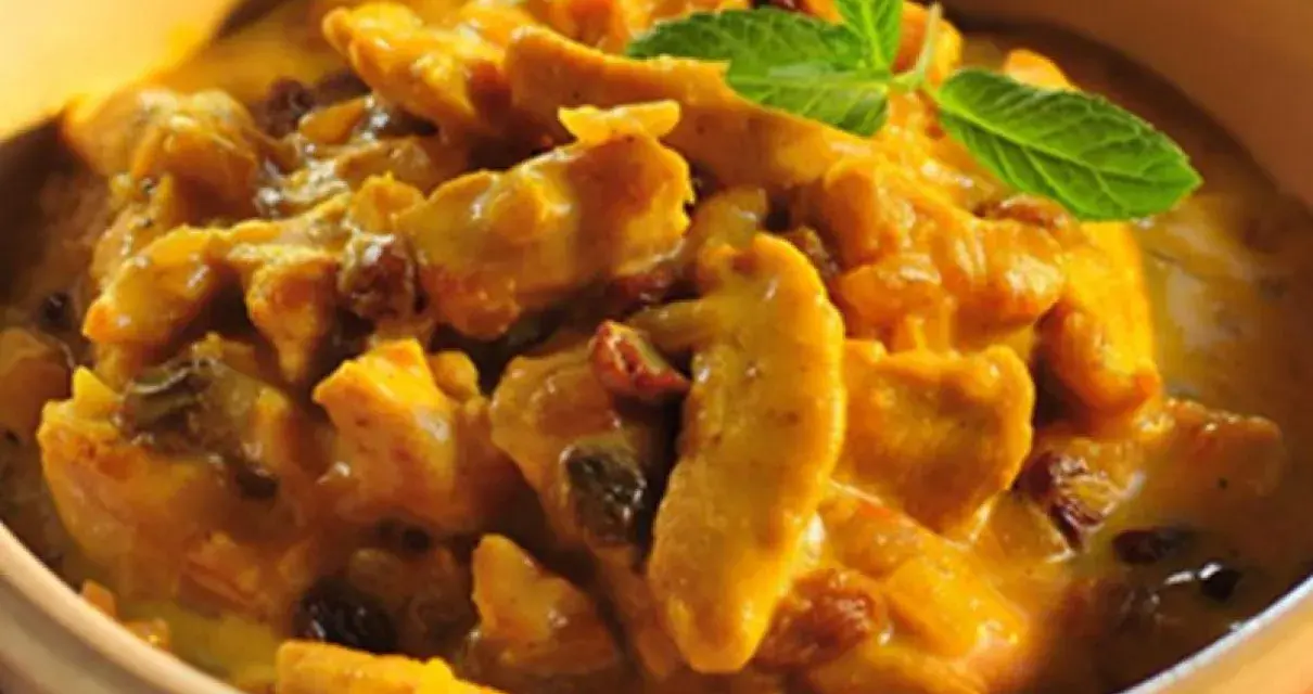 Pyszny kurczak w sosie curry z rodzynkami, ozdobiony listkiem mięty. Idealny przykład, jak zrobić sos curry do kurczaka.
