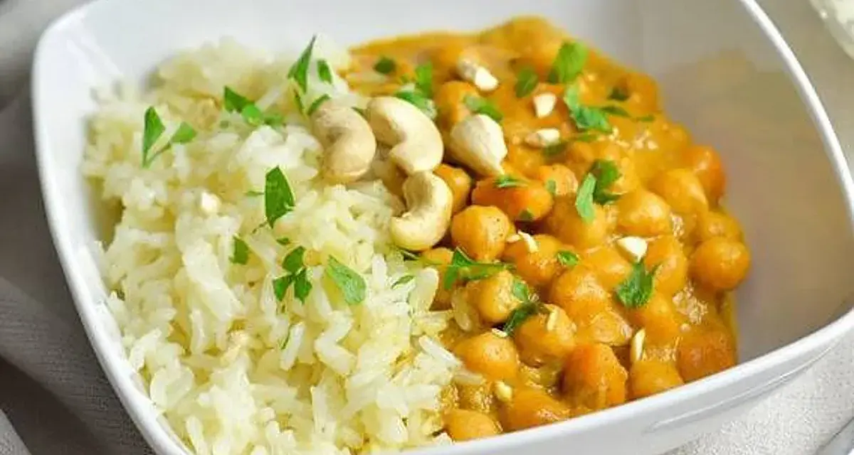 Curry de garbanzos cremoso con arroz blanco y anacardos en un cuenco blanco.
