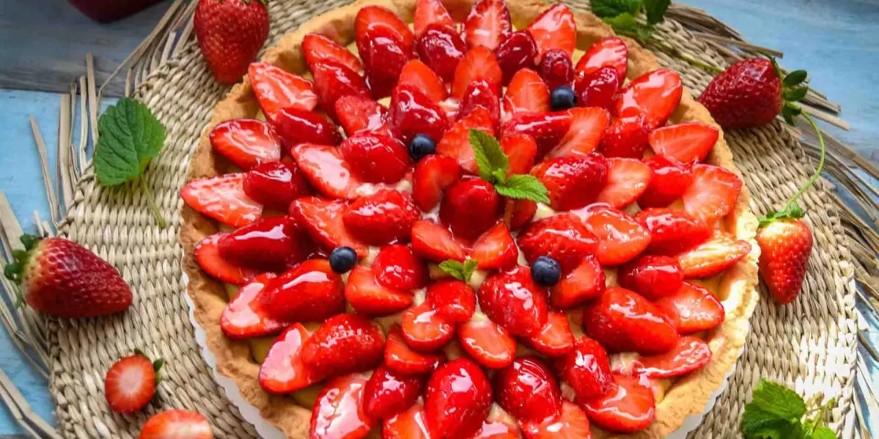 Ein leckerer Erdbeerkuchen mit einem wunderschönen Muster aus frischen Erdbeeren und Blaubeeren, glasiert und garniert mit Minze.