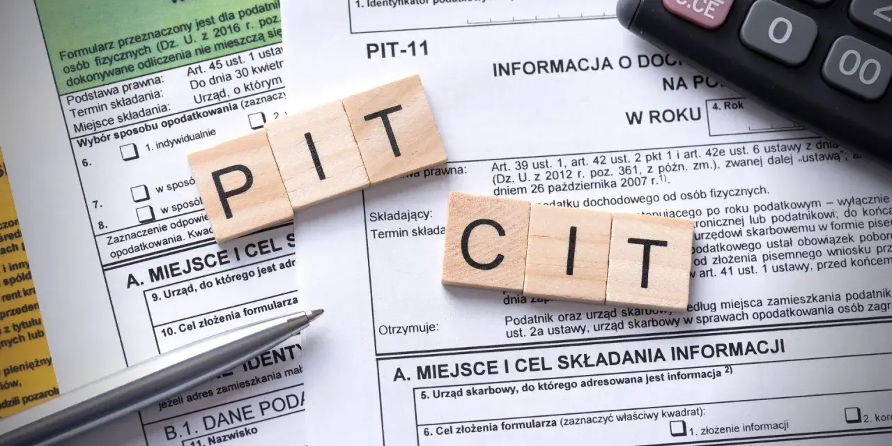 Drewniane klocki z literami "PIT" i "CIT" na formularzu podatkowym. Temat: podatek od sprzedaży nieruchomości po upływie 5 lat.