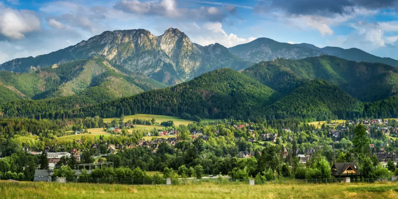 Malowniczy widok na Tatry z Jaszczurówki, gdzie liczne atrakcje czekają na turystów. Zielone wzgórza i tradycyjna zabudowa tworzą sielski krajobraz.
