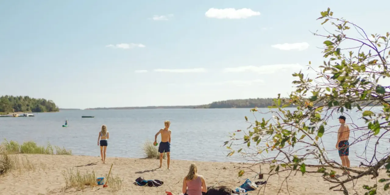 Solig dag vid Hallmare havsbad. Människor njuter på stranden, badar och leker i vattnet.