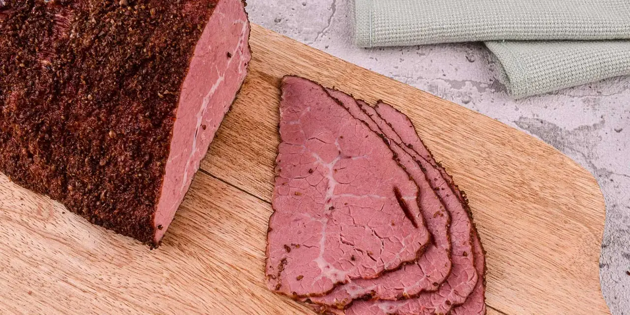 Pastrami co to? Aromatyczny, peklowany i wędzony kawałek wołowiny, pokrojony w cienkie plastry, leżący na desce.