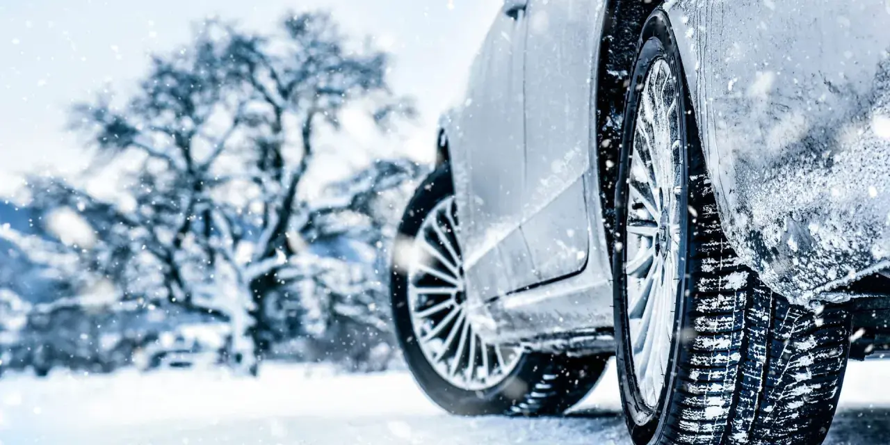 Auto im Schnee mit Winterreifen, verschneiter Baum im Hintergrund.