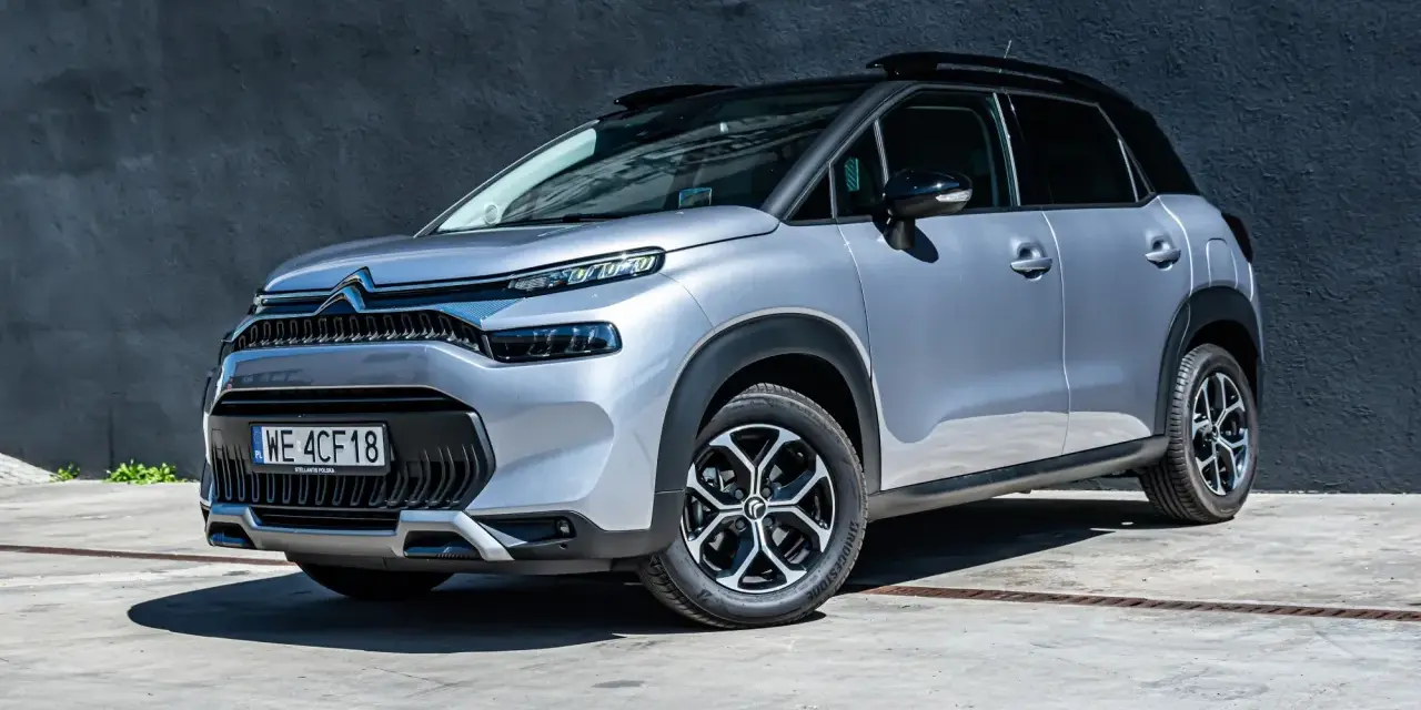 Srebrny Citroen C3 Aircross na tle ciemnej ściany. Wiele osób szuka **Citroen C3 Aircross opinie** przed zakupem.