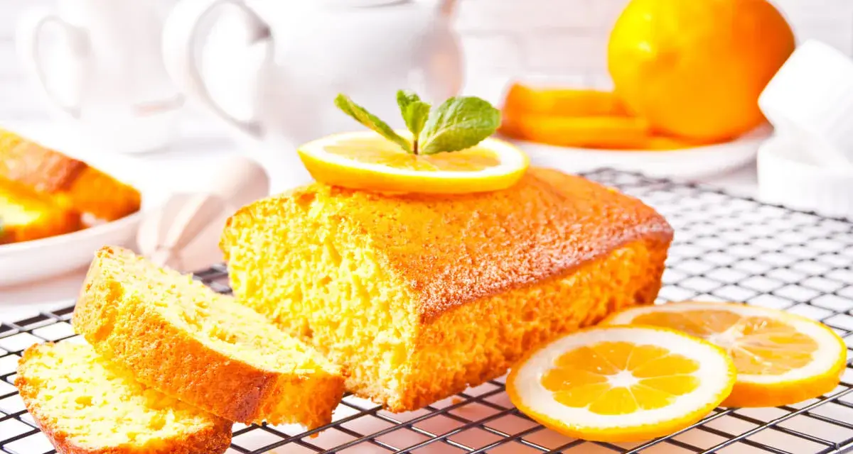 Un soffice plumcake al limone, guarnito con una fetta d'arancia e menta, su una griglia, pronto per essere gustato.