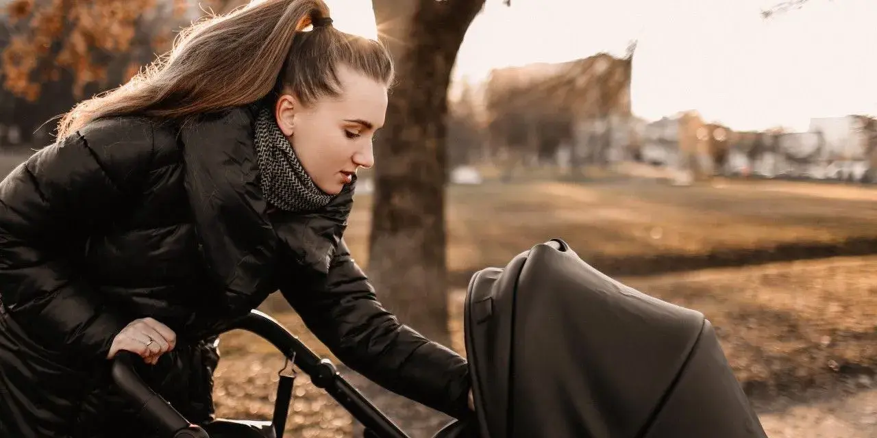 Mama przygotowuje malucha na spacer w 15 stopniach. Ciepła kurtka i szalik to podstawa, by zapewnić komfort dziecku w wózku.