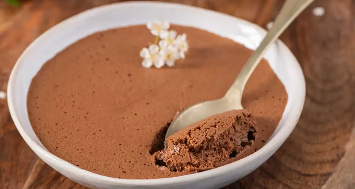 Une cuillère prend une bouchée d'une mousse au chocolat facile et aérienne, garnie de petites fleurs blanches.